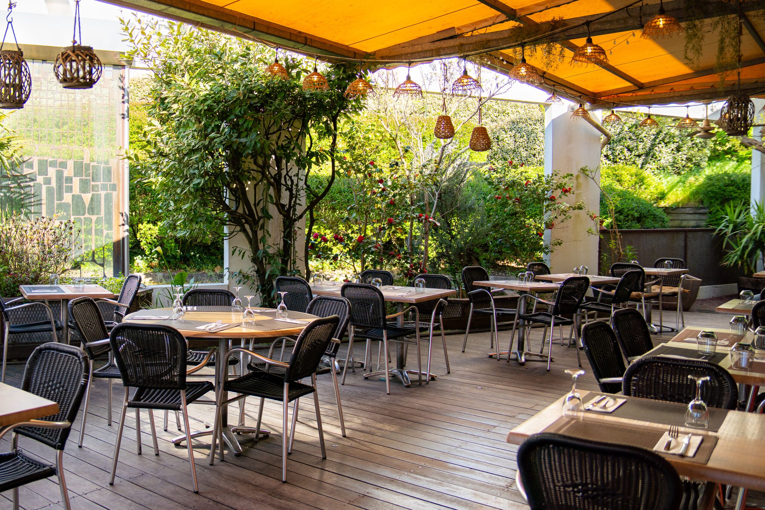 Terrasse arborée de Meltin’Potes Caffé, avec ses tables dressées et ses suspensions en osier.